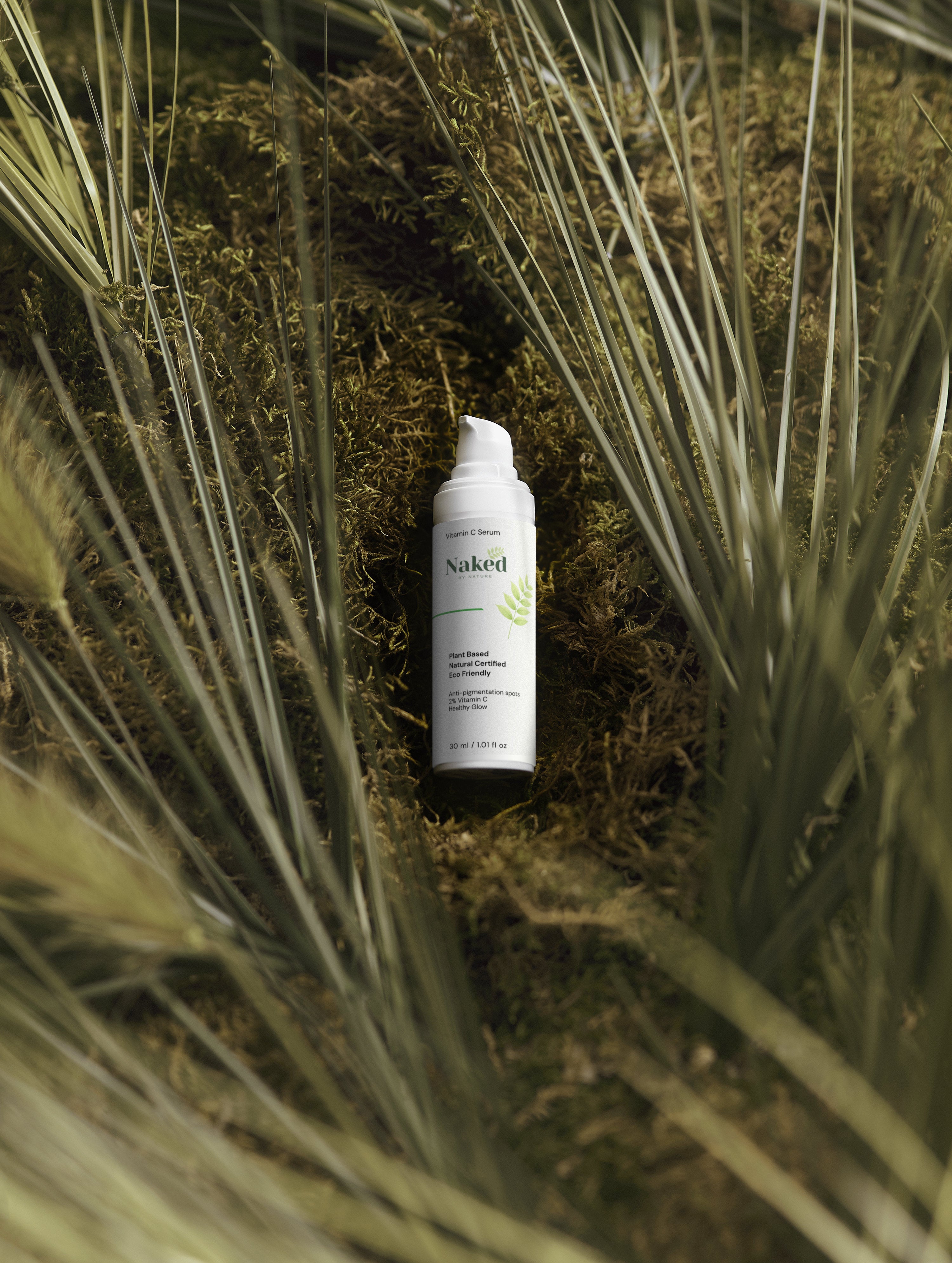 Naked by Nature Vitamin C Serum bottle nestled in moss and grass, plant-based skincare for healthy glow