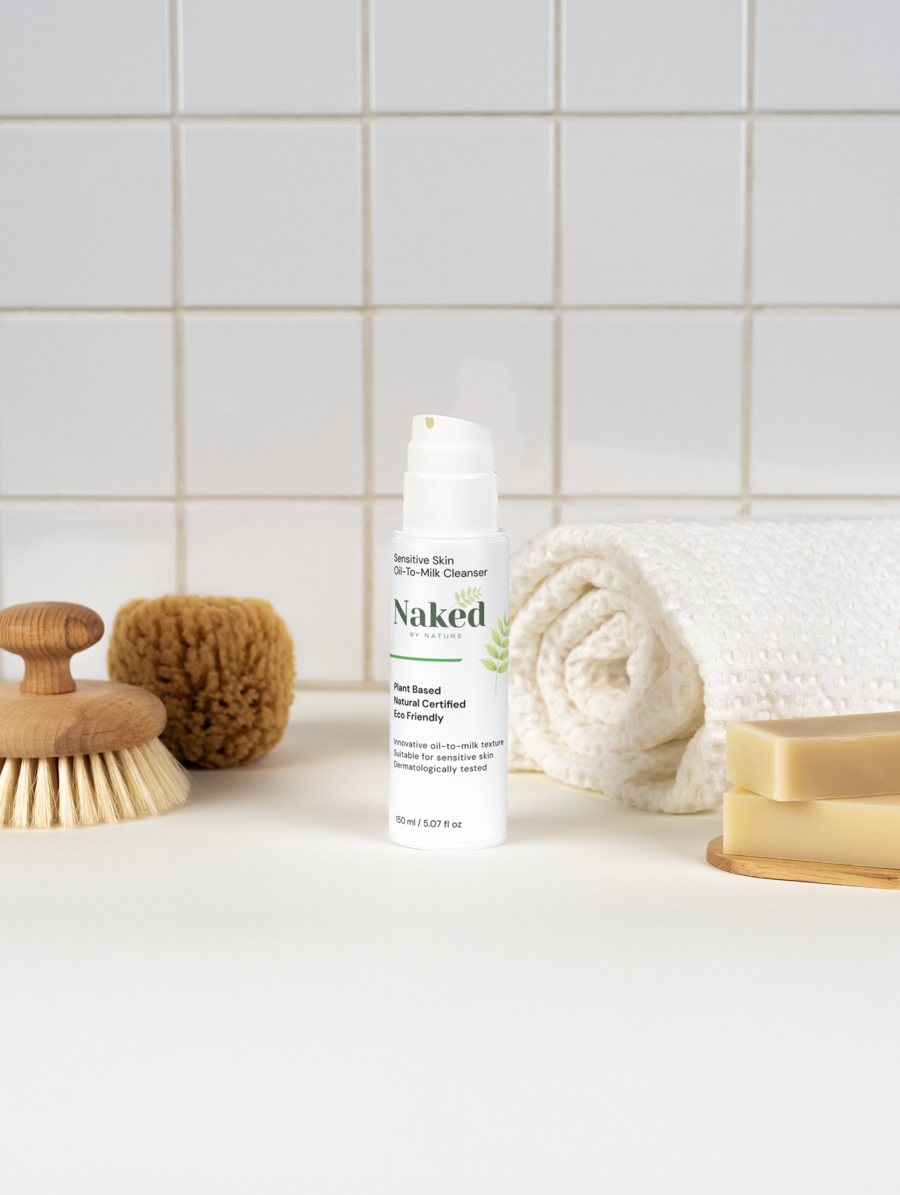 Sensitive skin oil-to-milk cleanser, plant-based & eco-friendly, with natural soap and bath brush on white tiles