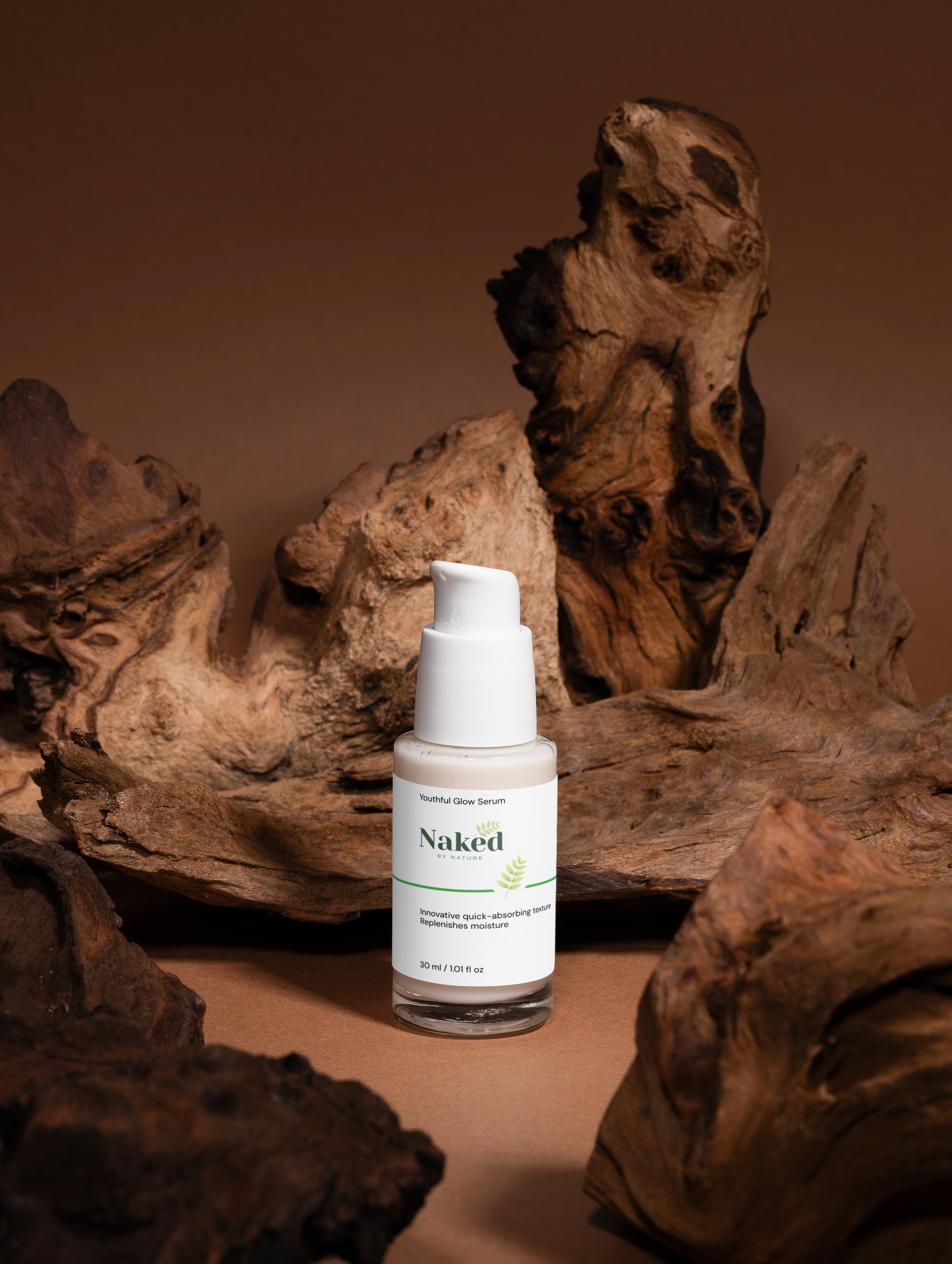 Youthful Glow Serum in glass bottle with white pump, surrounded by natural driftwood, plant-based skincare