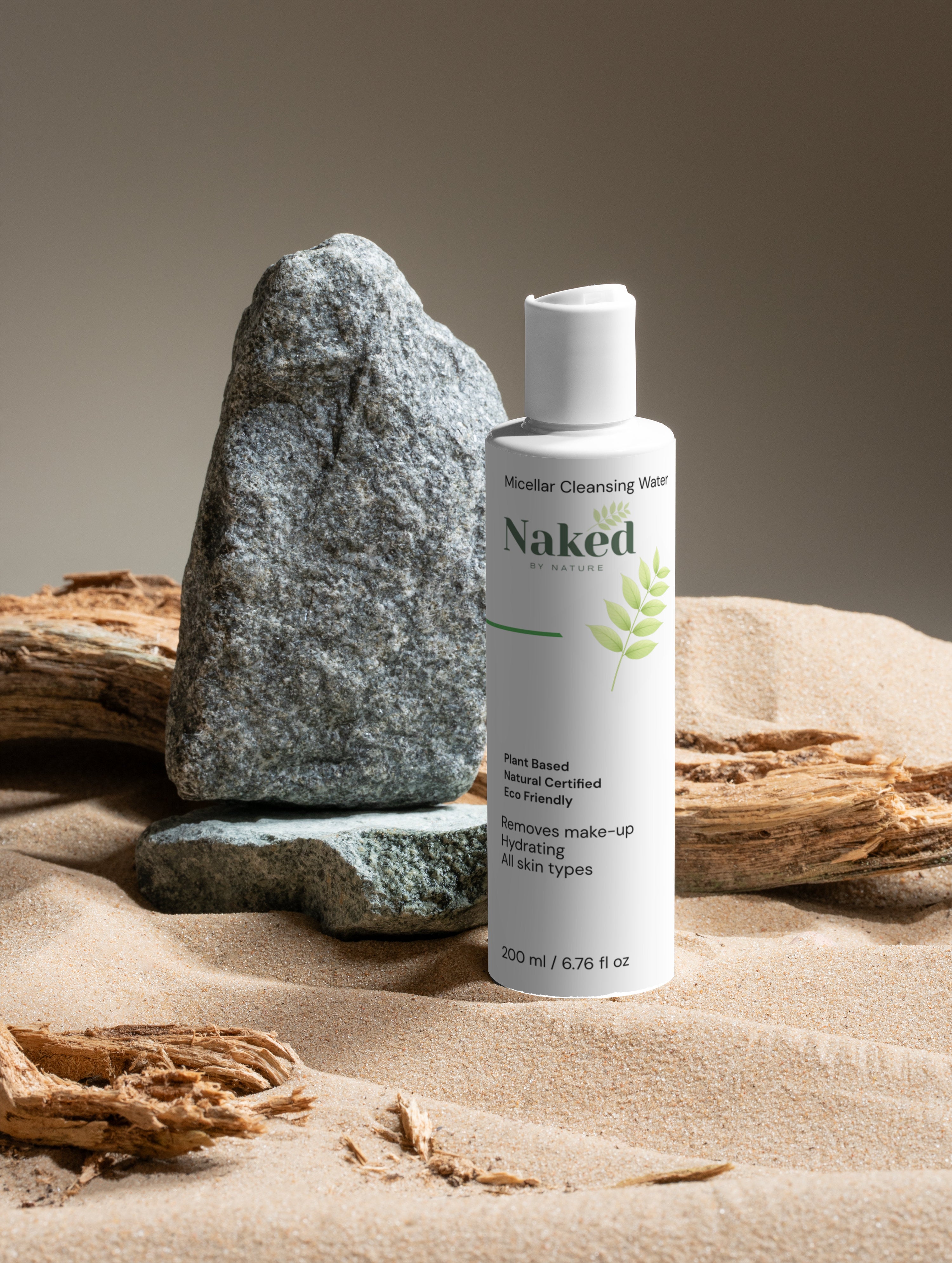 Naked by Nature Micellar Cleansing Water bottle on sand with rocks, plant-based, hydrating, removes makeup for all skin types