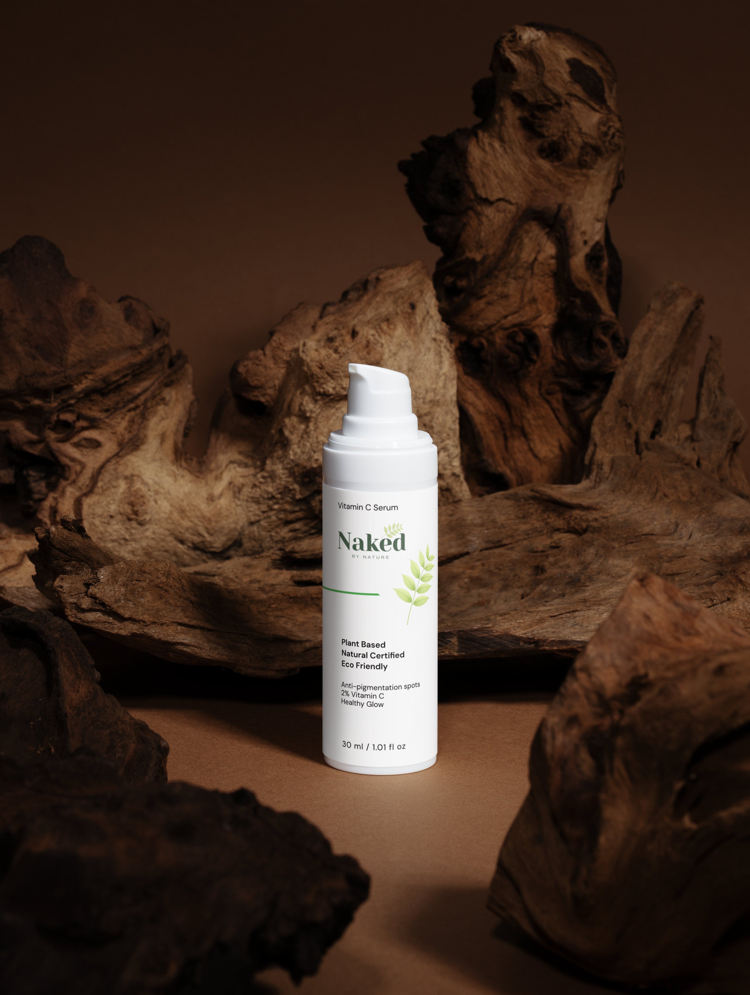 Naked By Nature Vitamin C Serum bottle with plant-based, eco-friendly skincare label, set against rustic driftwood background