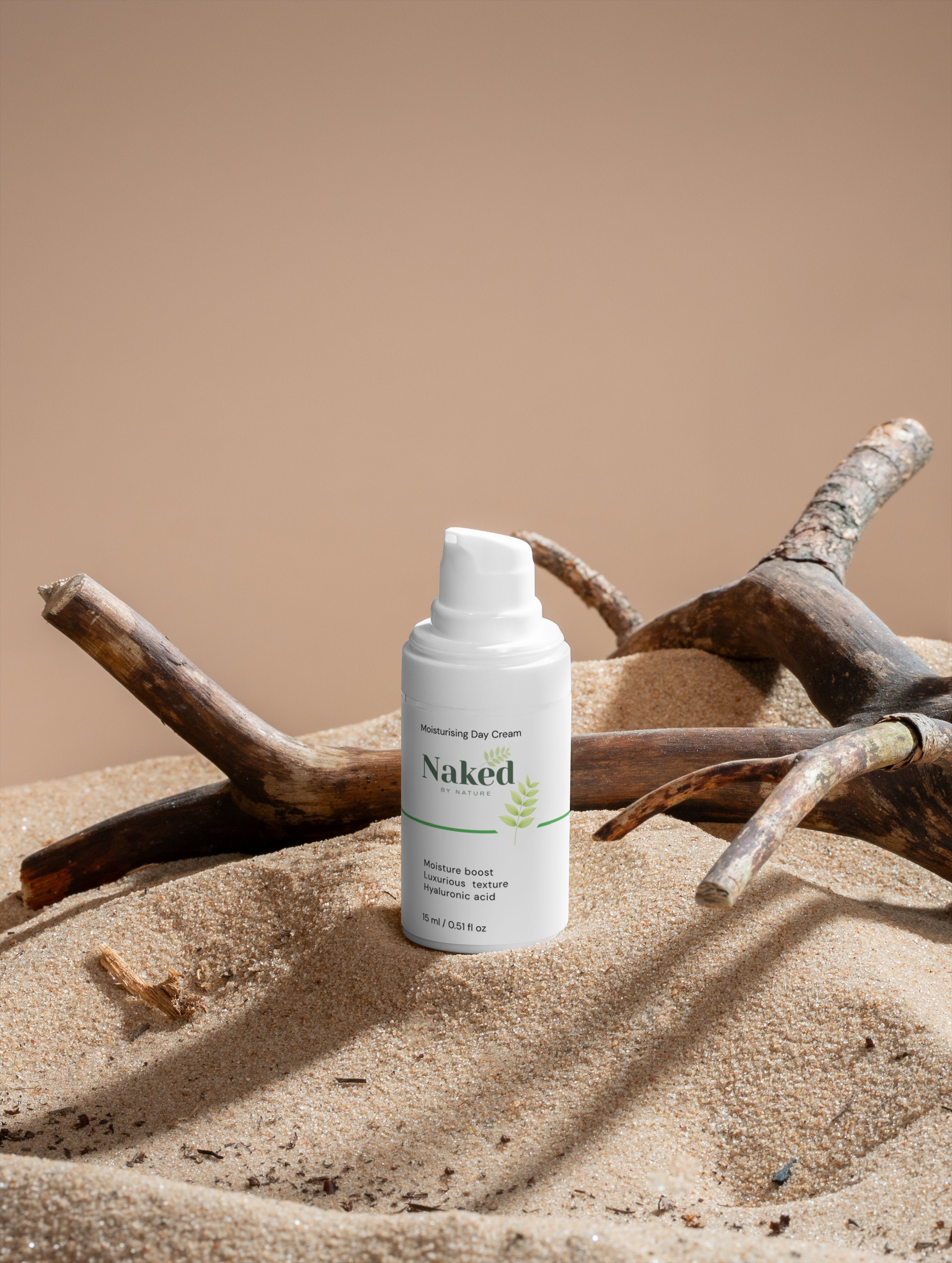 Naked by Nature Moisturising Day Cream with hyaluronic acid, nestled in sand with driftwood, for gentle plant-based skincare.