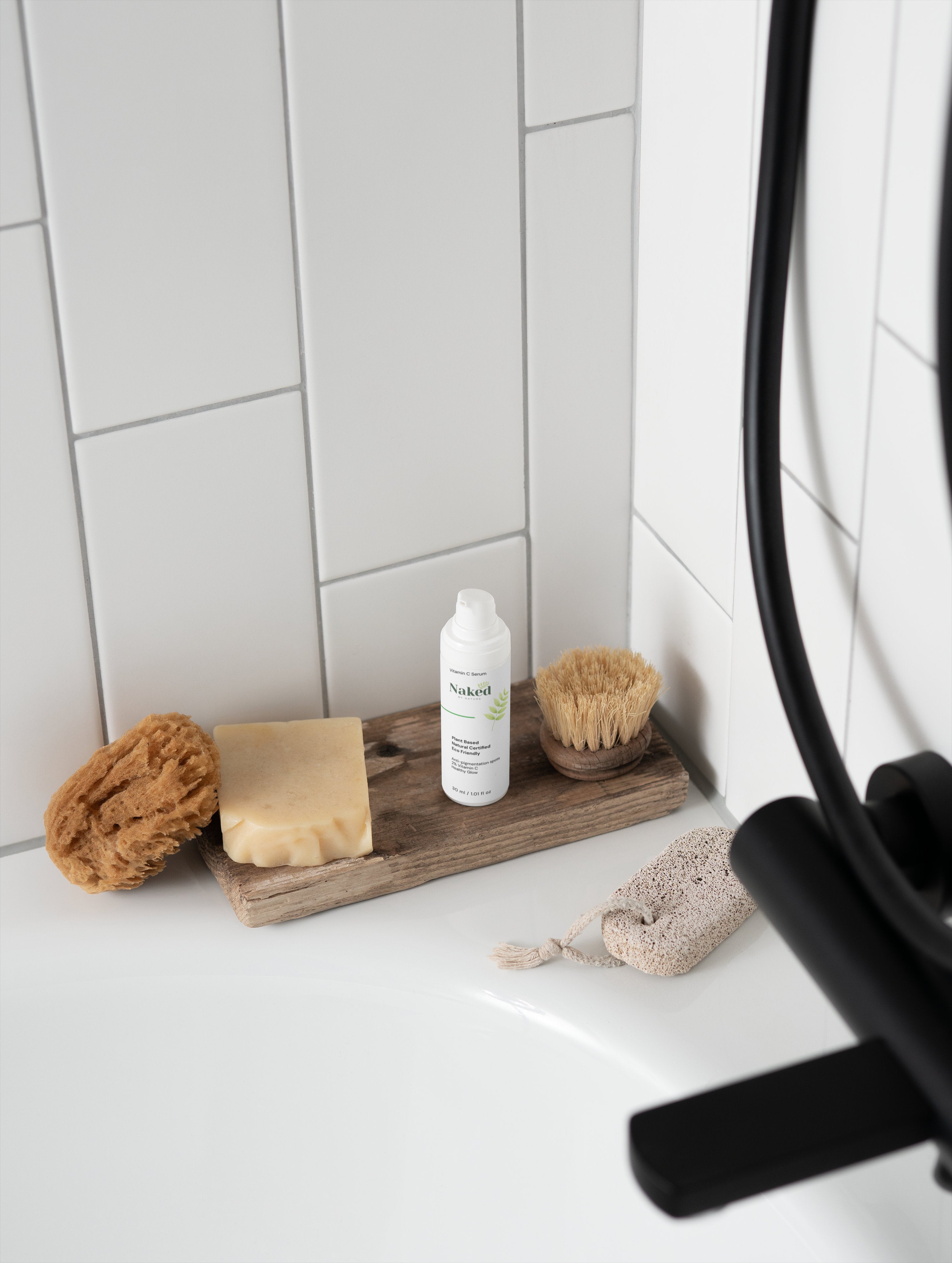 Plant-based Vitamin C serum with natural soap and eco-friendly bath tools on wooden tray in white tiled bathroom