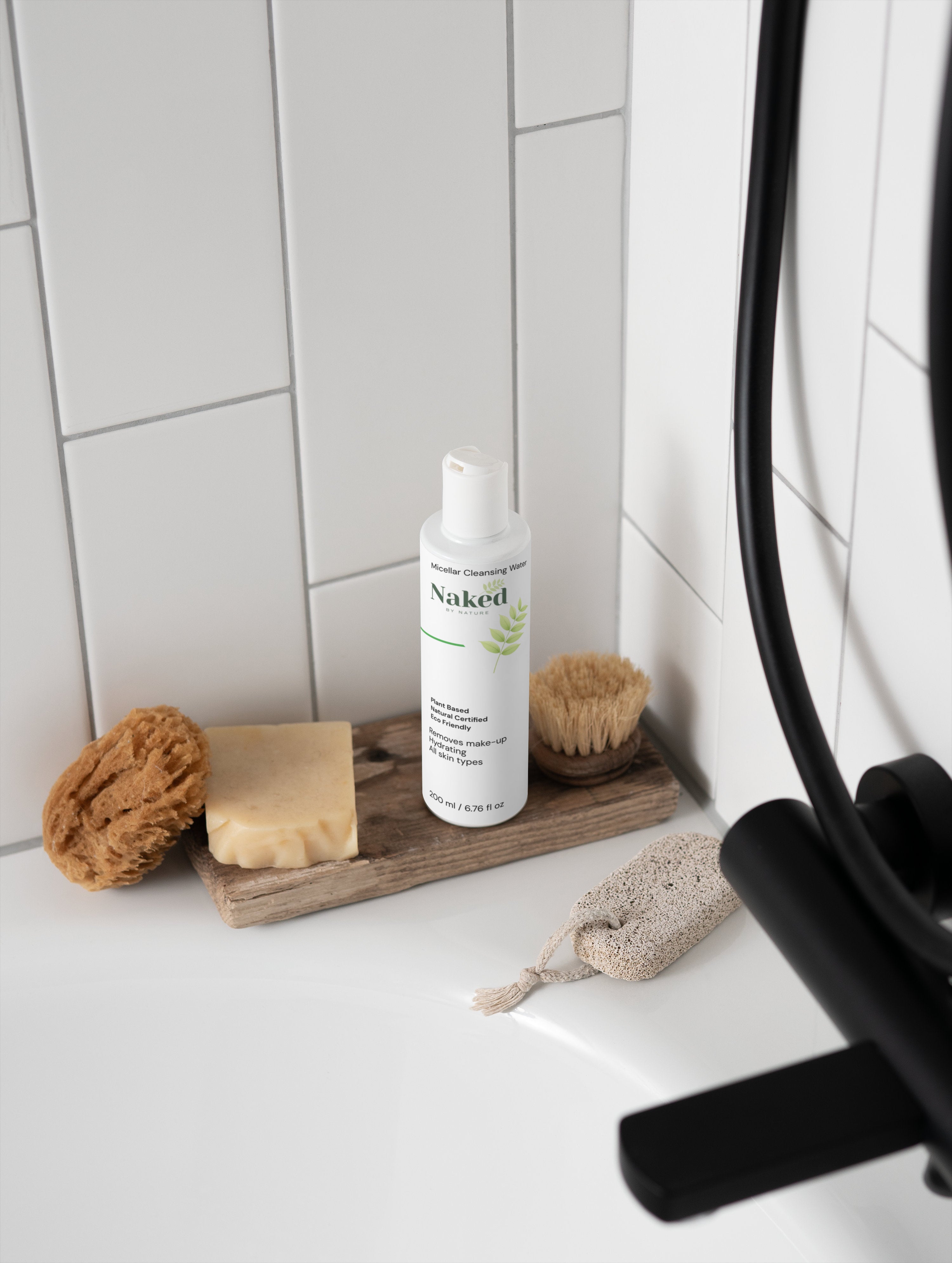 Naked by Nature Micellar Cleansing Water bottle with natural soap, sponge, and brush on wooden tray in bathroom